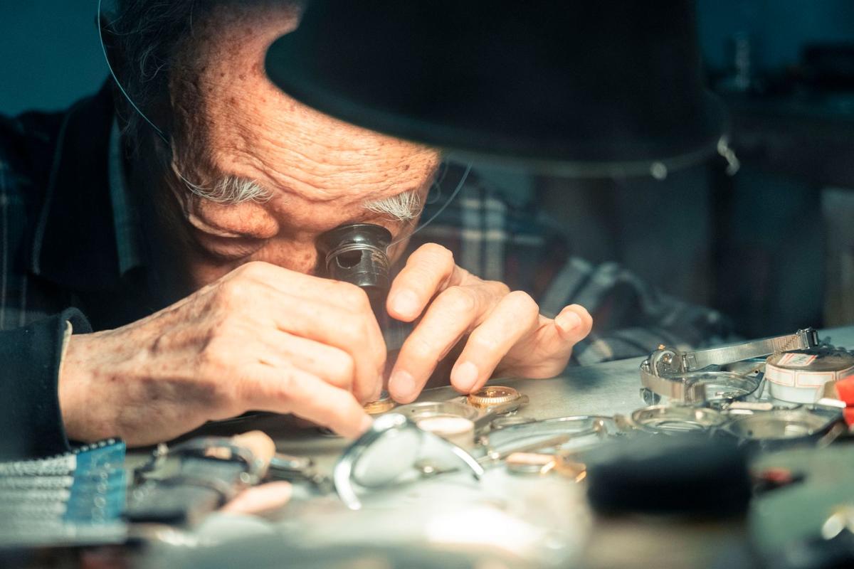 A watchmaker inspecting a watch through a loupe at his bench